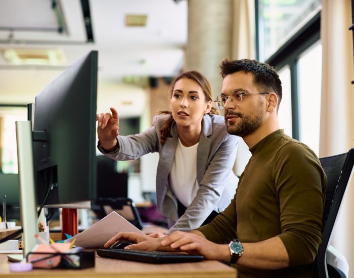 Young colleagues cooperating while working on a computer in the office.